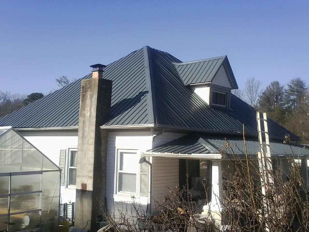 Dark blue standing seam metal roof on a white farmhouse with dormer — Slate & Tile Roof Repair by Roofing Brothers in White Haven