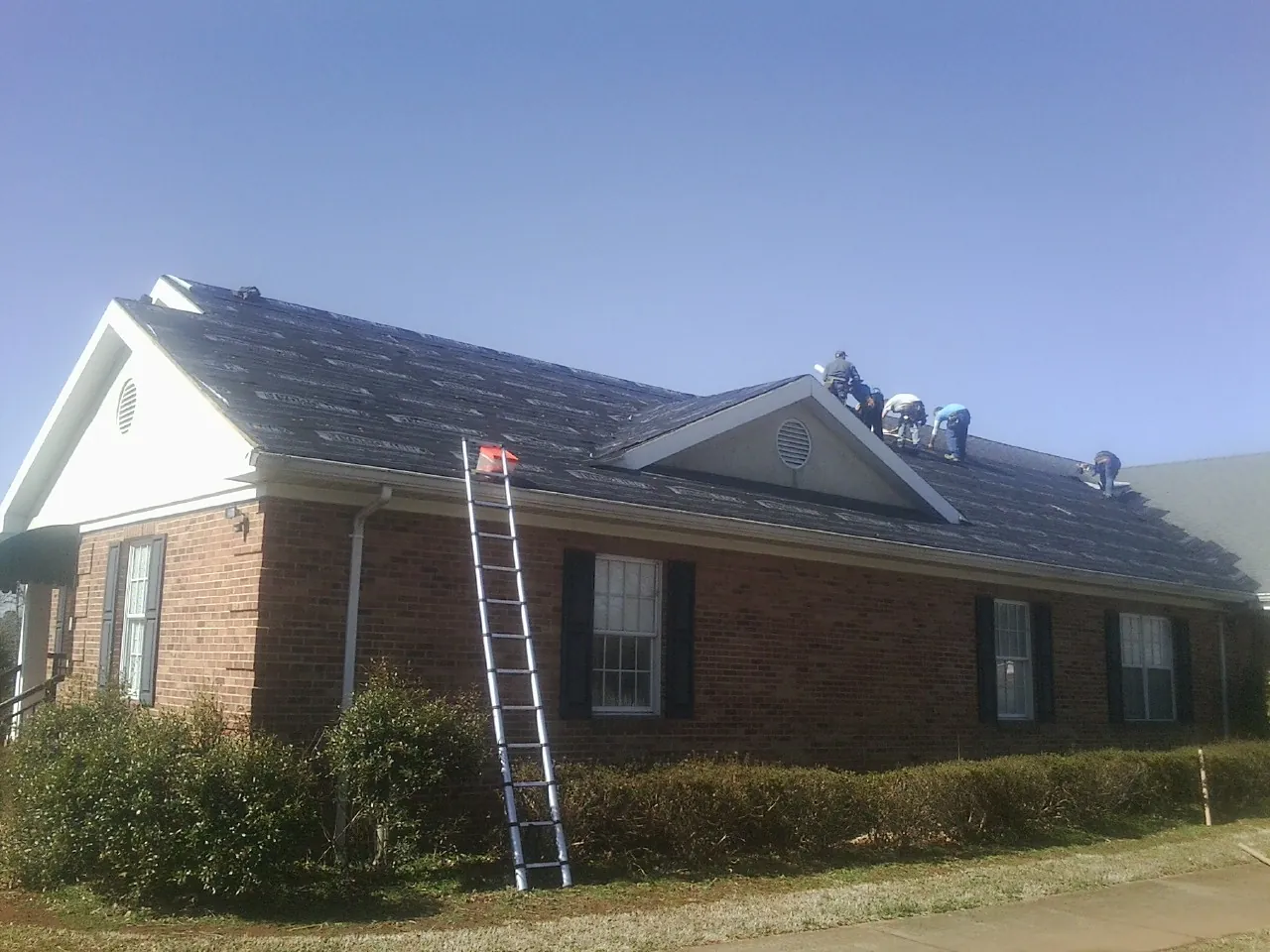 Crew tearing shingles off a brick ranch roof with a ladder set — Metal Roof Repair work by our crew in White Haven