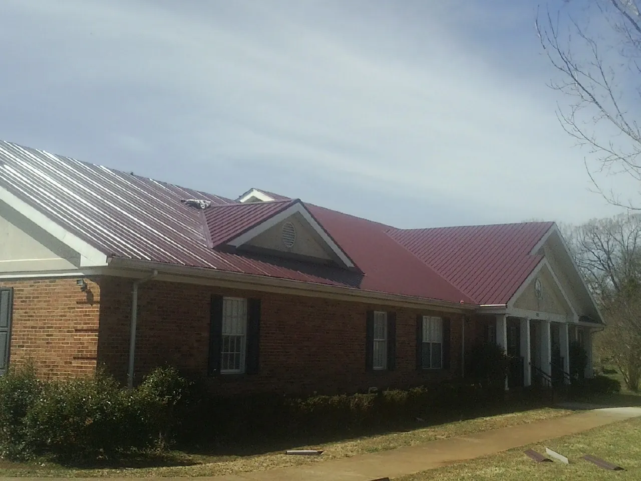 Red metal roof with gabled entries on a long brick building, from a Hail Damage Roof Repair job in White Haven