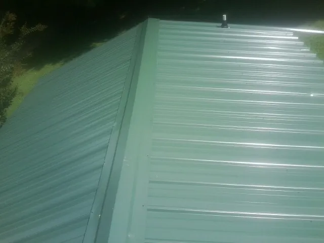 New green metal panels meeting at the ridge of a roof — Flat Roof Repair work by our crew in White Haven