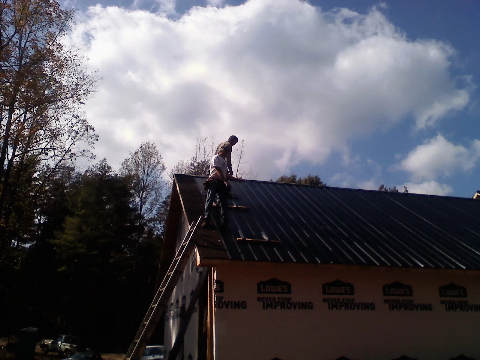 Roofer fastening dark metal panels high against a cloudy sky, from a Roof Inspection job in White Haven