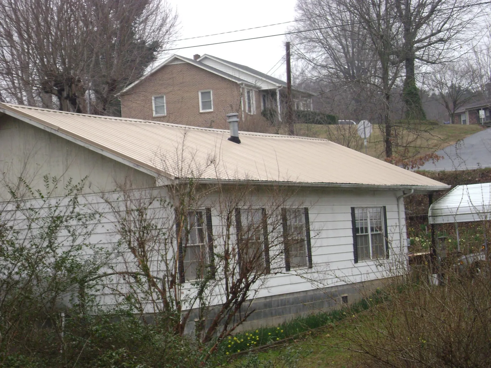 Tan metal roof on a white sided house set into a hillside — Commercial Roofing by Roofing Brothers in White Haven